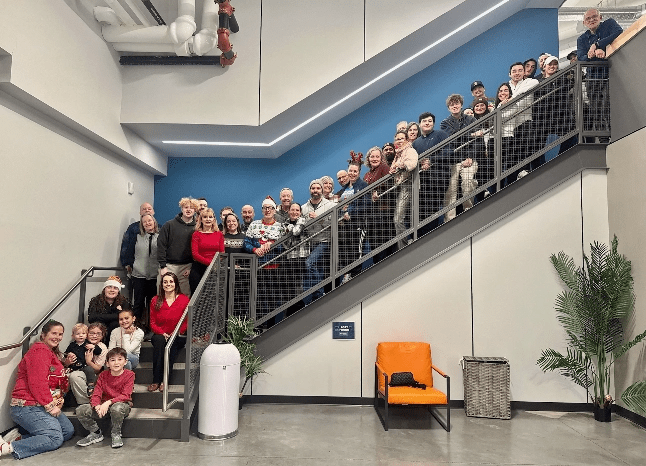Large group of people wearing festive hats posing on and around a diagonal stairwell in a bright, modern building.