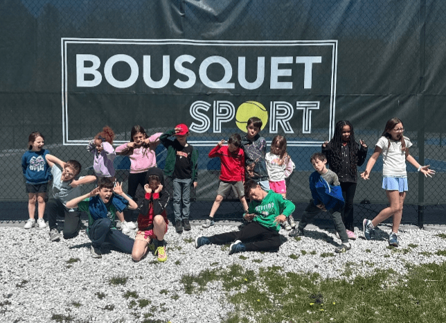 Group of children posing together in front of a Bousquet Sport banner outdoors.